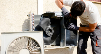 young man electrician installer working on outdoor compressor unit air conditioner at a client's home